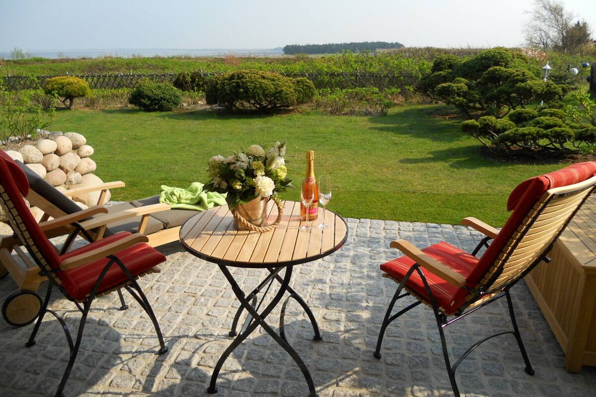 Eine Terrasse mit einem runden Tisch, zwei roten Sitzgelegenheiten, einer Champagnerflasche und einem Blumenstrauß.