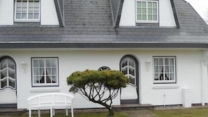 A white house with a sloped roof, multiple windows, and a small tree in the front yard. - Ferienwohnung Sönshörn 8 Mitte (Sylt)
