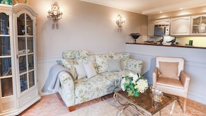 A living room with a floral sofa, a glass coffee table, a beige armchair, and a white cabinet with glass doors. - Ferienwohnung Sönshörn 8 Mitte (Sylt)