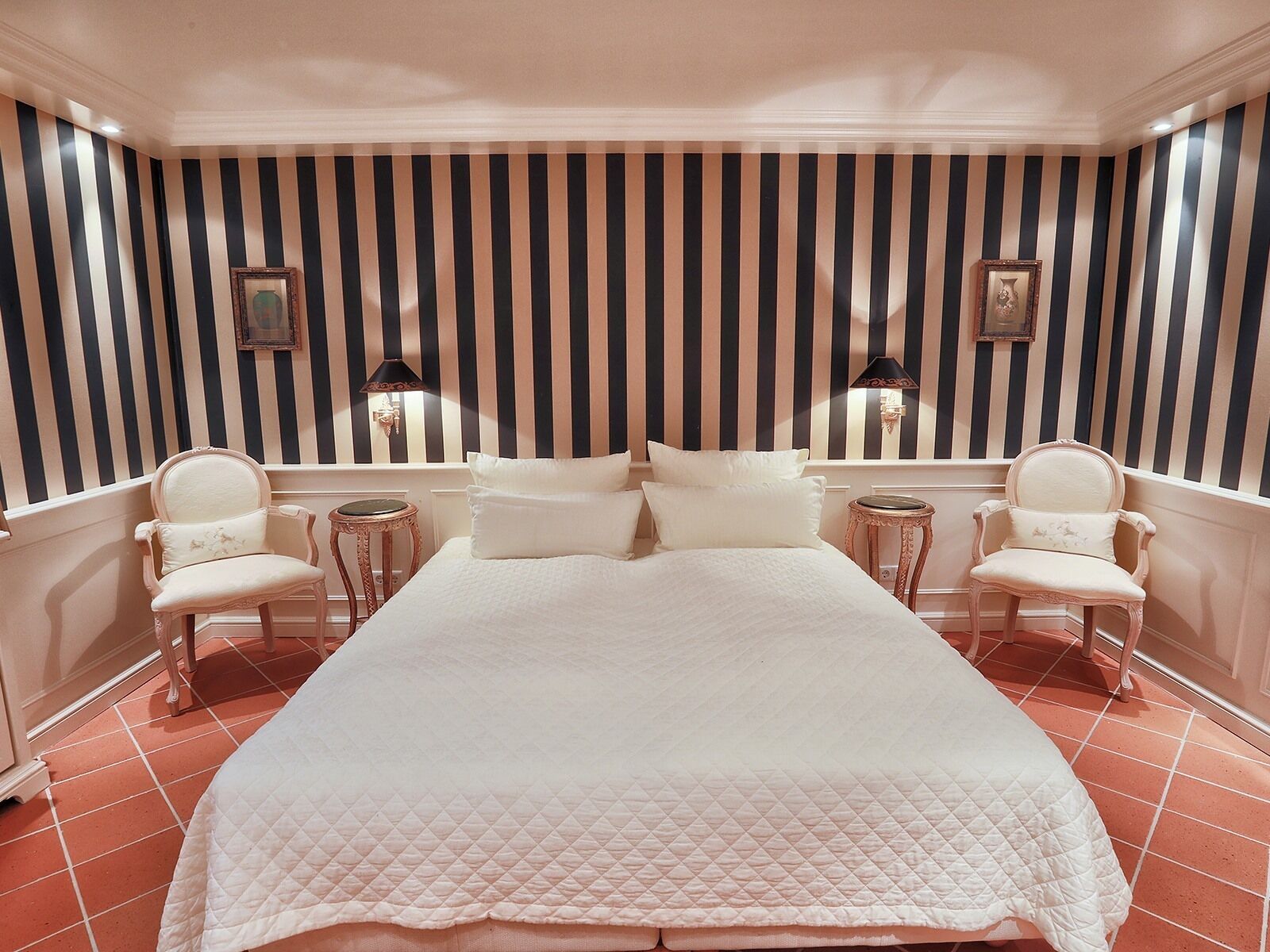 A hotel room with a large bed, two chairs, a small table, and striped wallpaper.