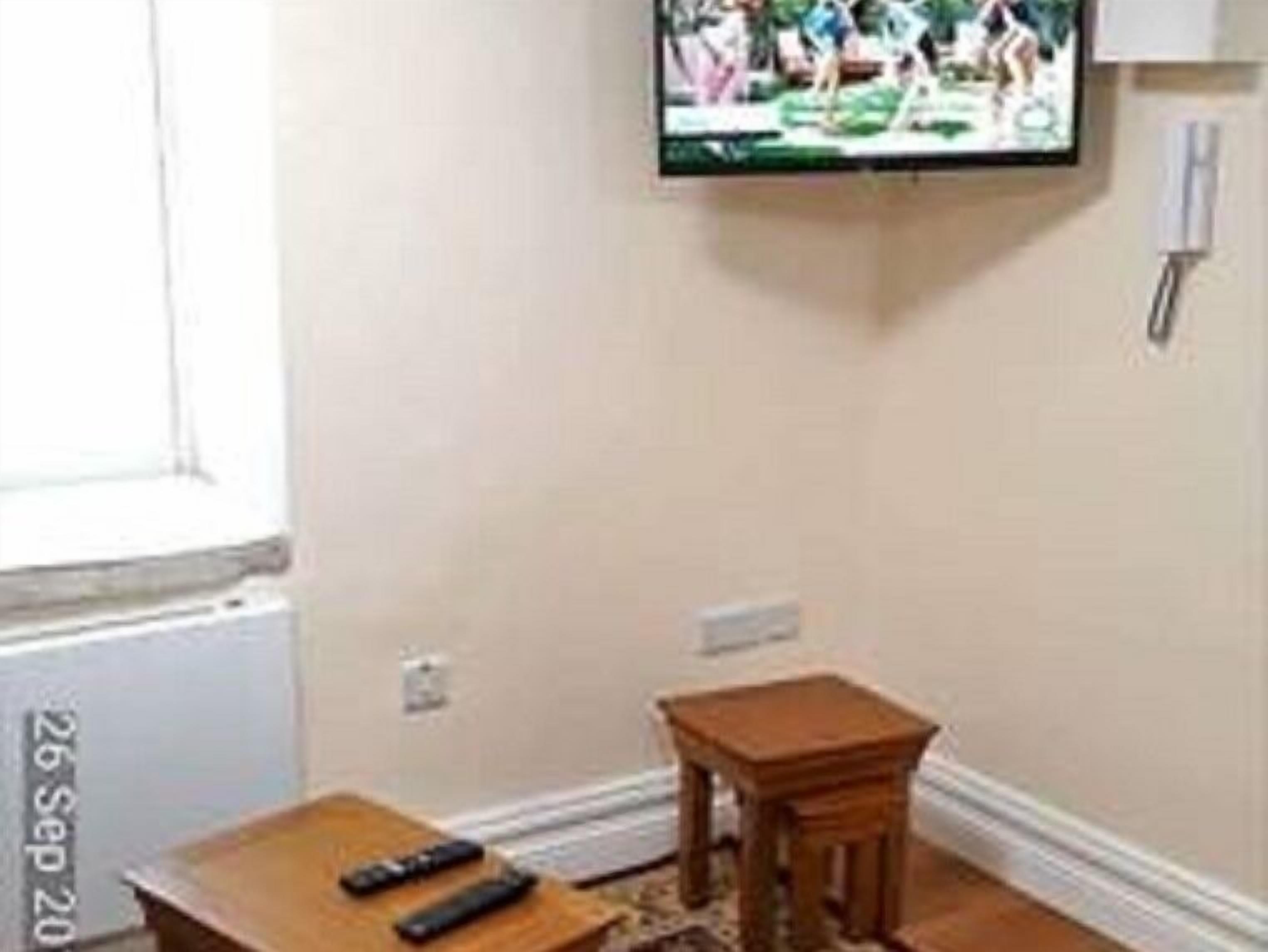 A room with a television mounted on the wall, a small wooden table, and a window with a view of the outdoors.