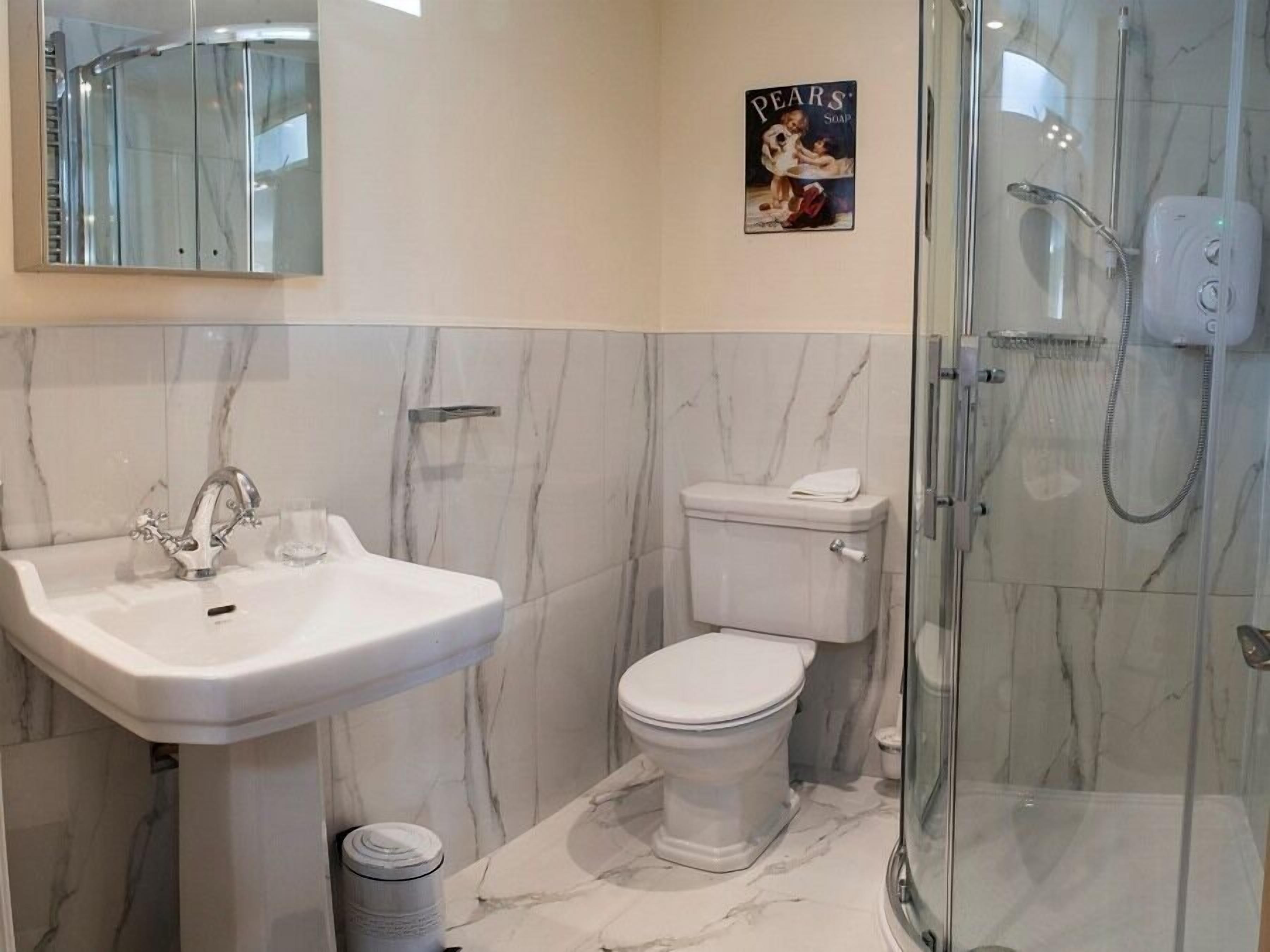 Une salle de bain avec un sol en marbre, un lavabo blanc, des toilettes et une douche à parois de verre.