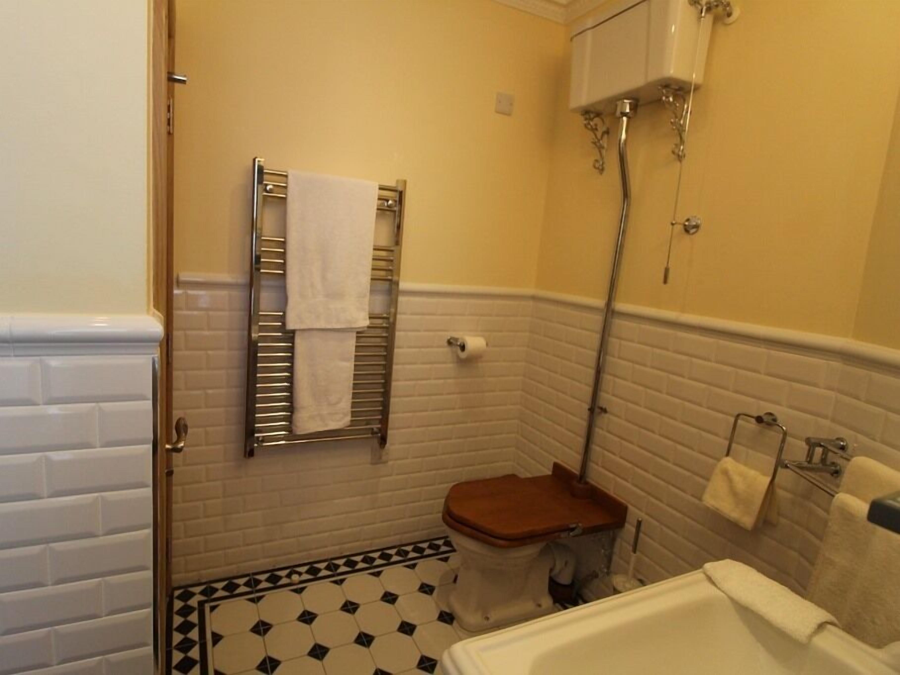 A small bathroom with a toilet, a sink, and a bathtub. There is a towel rack with a towel hanging on it. The walls are tiled, and there is a showerhead above the bathtub.