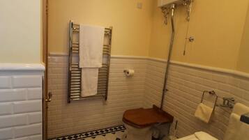 A small bathroom with a toilet, a sink, and a bathtub. There is a towel rack with a towel hanging on it. The walls are tiled, and there is a showerhead above the bathtub.