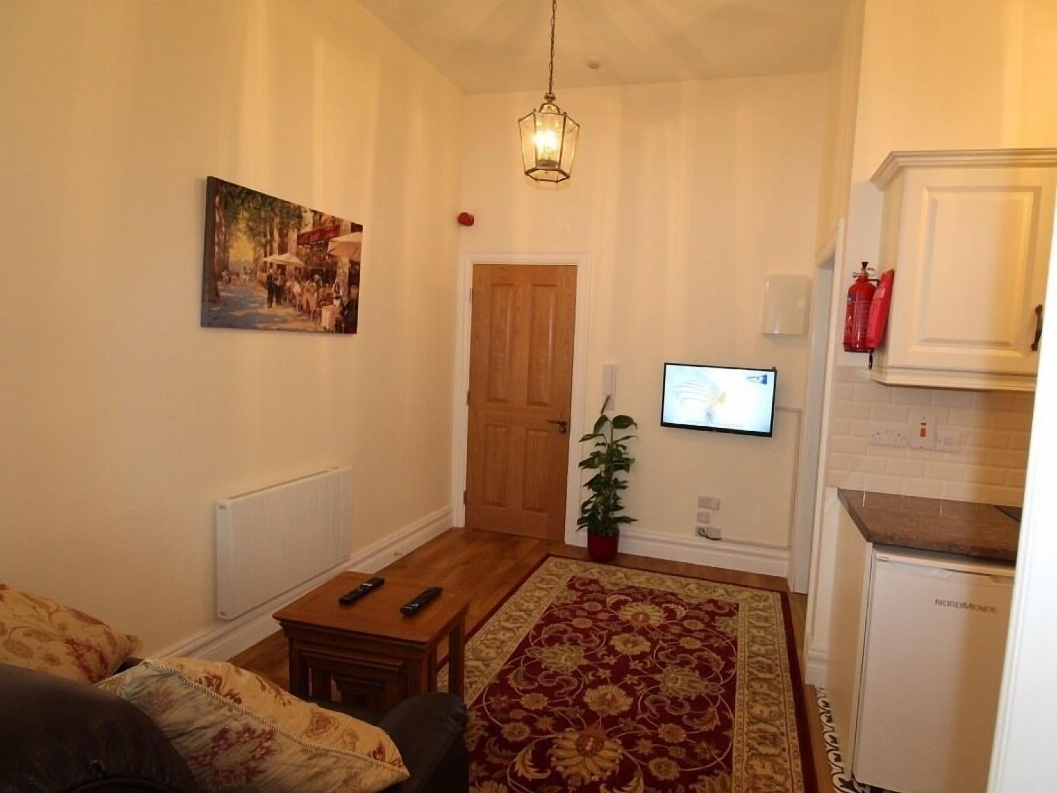 A living room with a sofa, a coffee table, a TV mounted on the wall, a wooden door, and a small plant.
