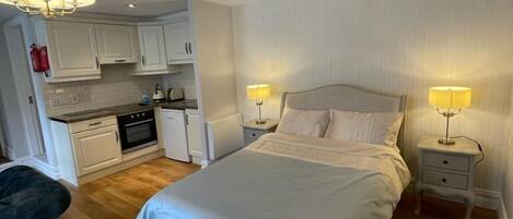 Un dormitorio con una cama grande, mesitas de noche con lámparas, una kitchenette y una silla.