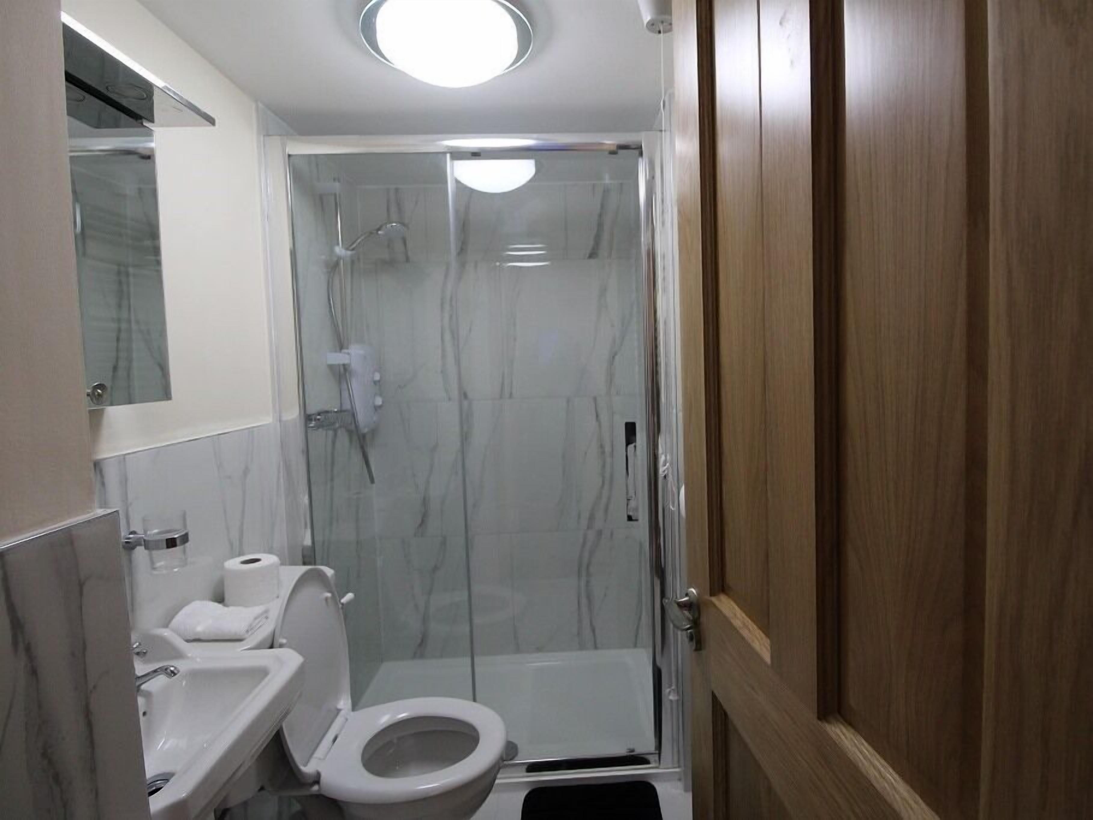 A compact bathroom with a shower, toilet, sink, and mirror.