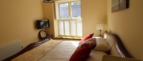 A hotel room with a large bed, a television on the wall, a window with blinds, and a painting above the bed.