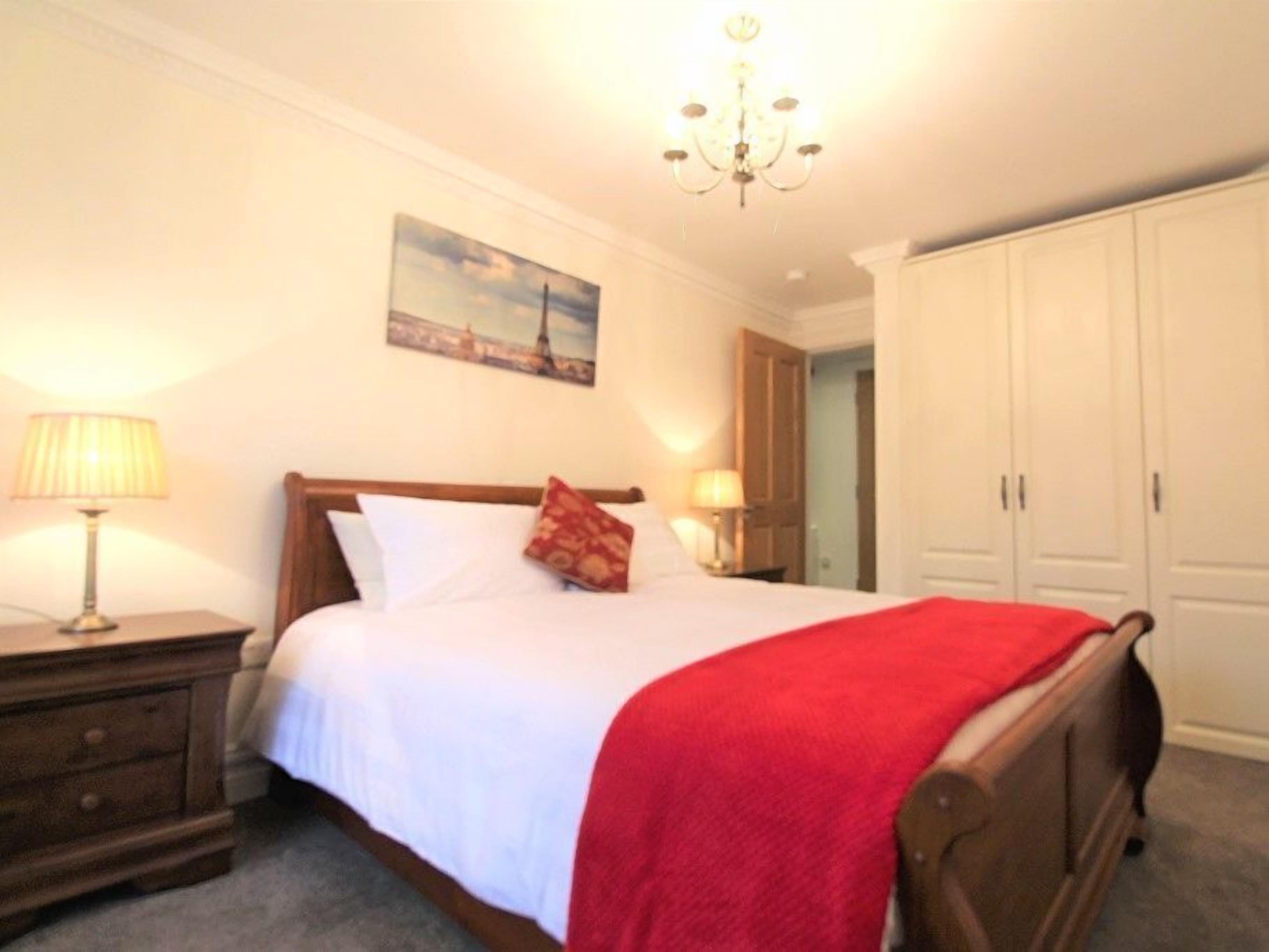 A bedroom with a bed, a nightstand, a lamp, a painting, and a wardrobe.