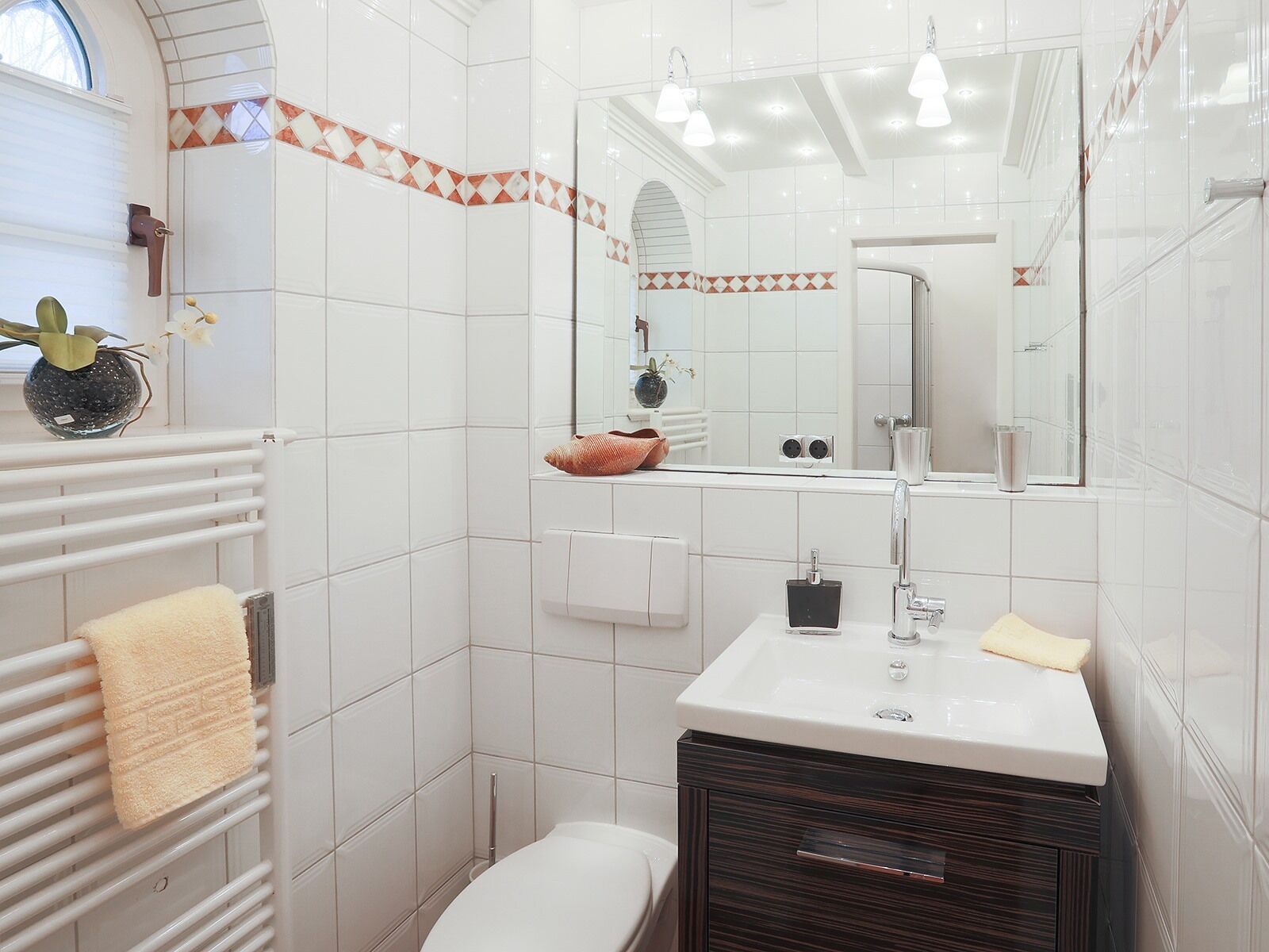 A modern bathroom with white tiles, a vanity with a mirror, a toilet, and a towel rack.