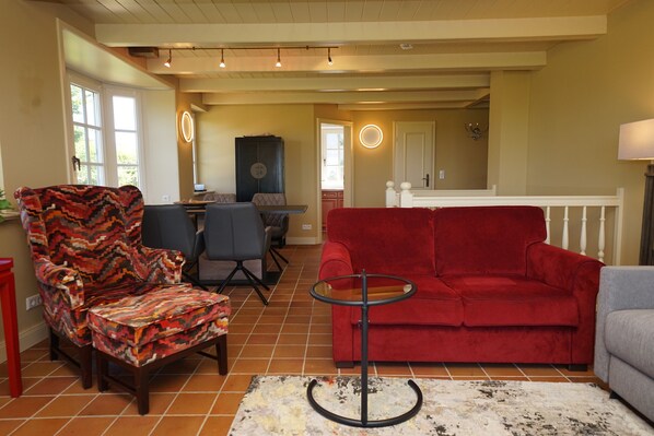 Un salón con un sofá rojo, un sillón estampado y una pequeña mesa redonda. Se ve una escalera que conduce a un nivel superior.