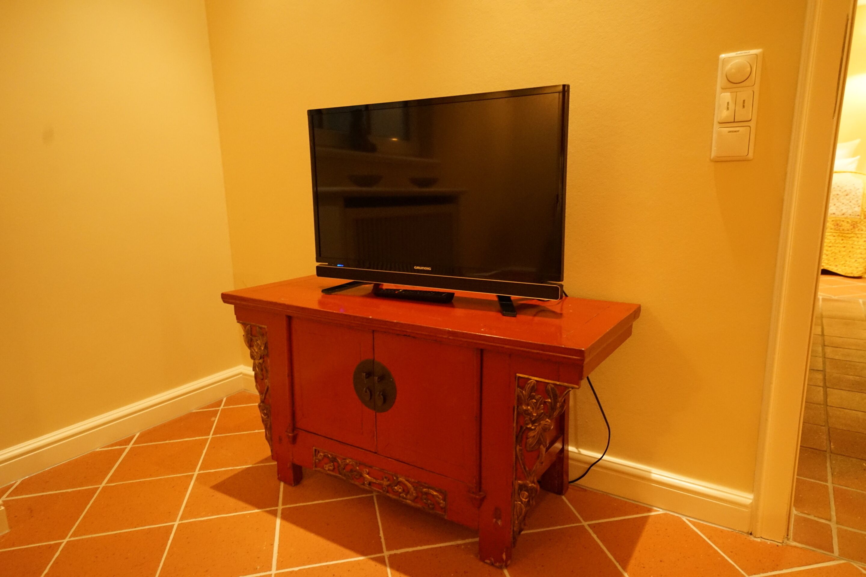 A television on a wooden cabinet in a room with orange-tiled flooring.