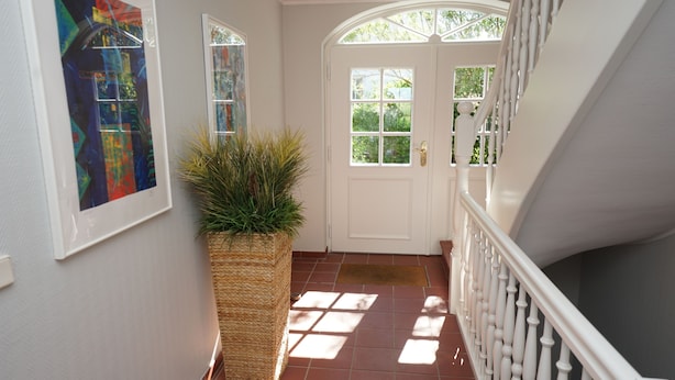 Un couloir avec une porte blanche, une plante en pot et un escalier avec des balustrades blanches.