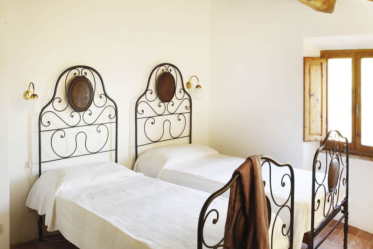 A bedroom with two beds, a wooden window, and a white wall.