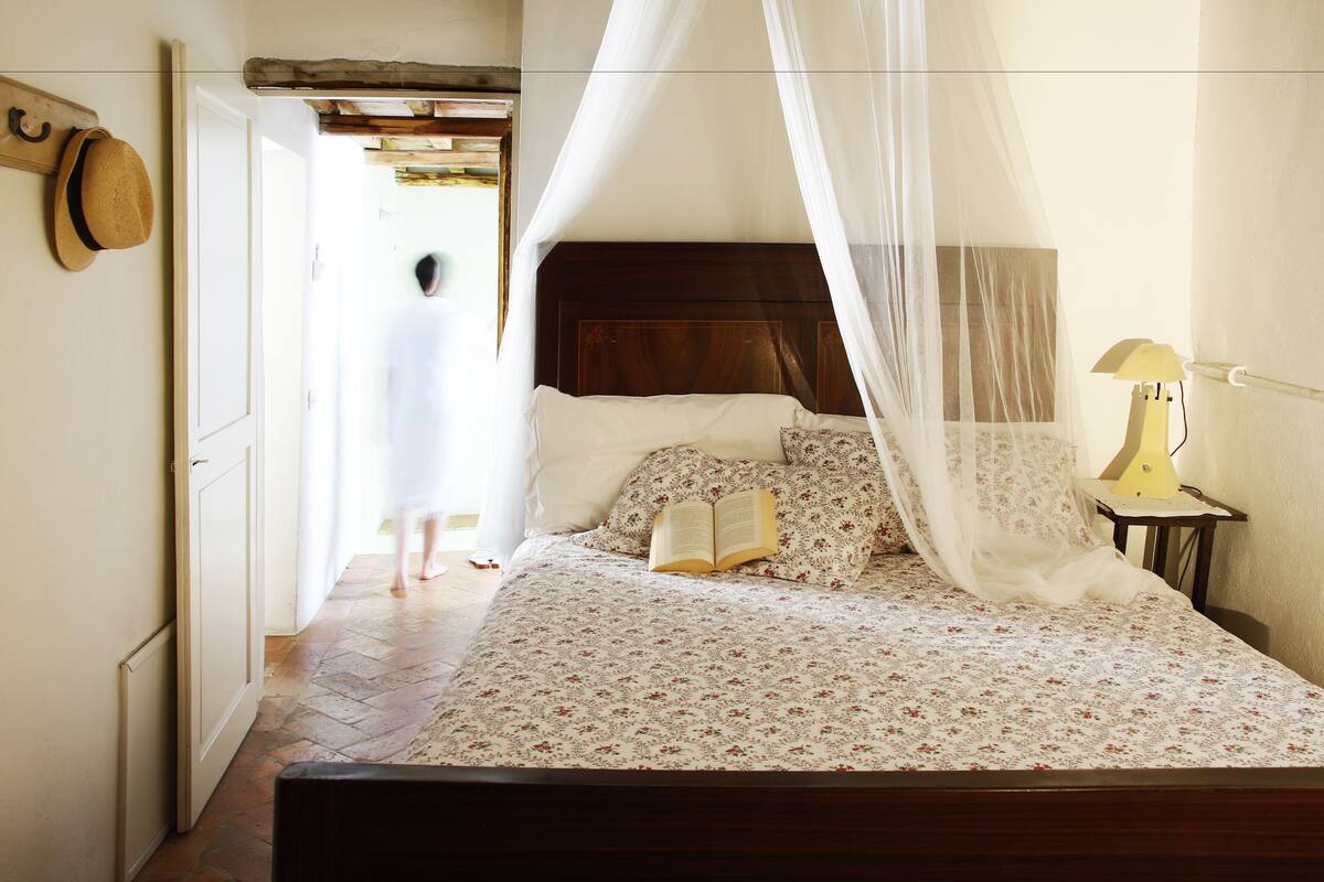 A bedroom with a bed, a nightstand, a lamp, and a hat on the wall.