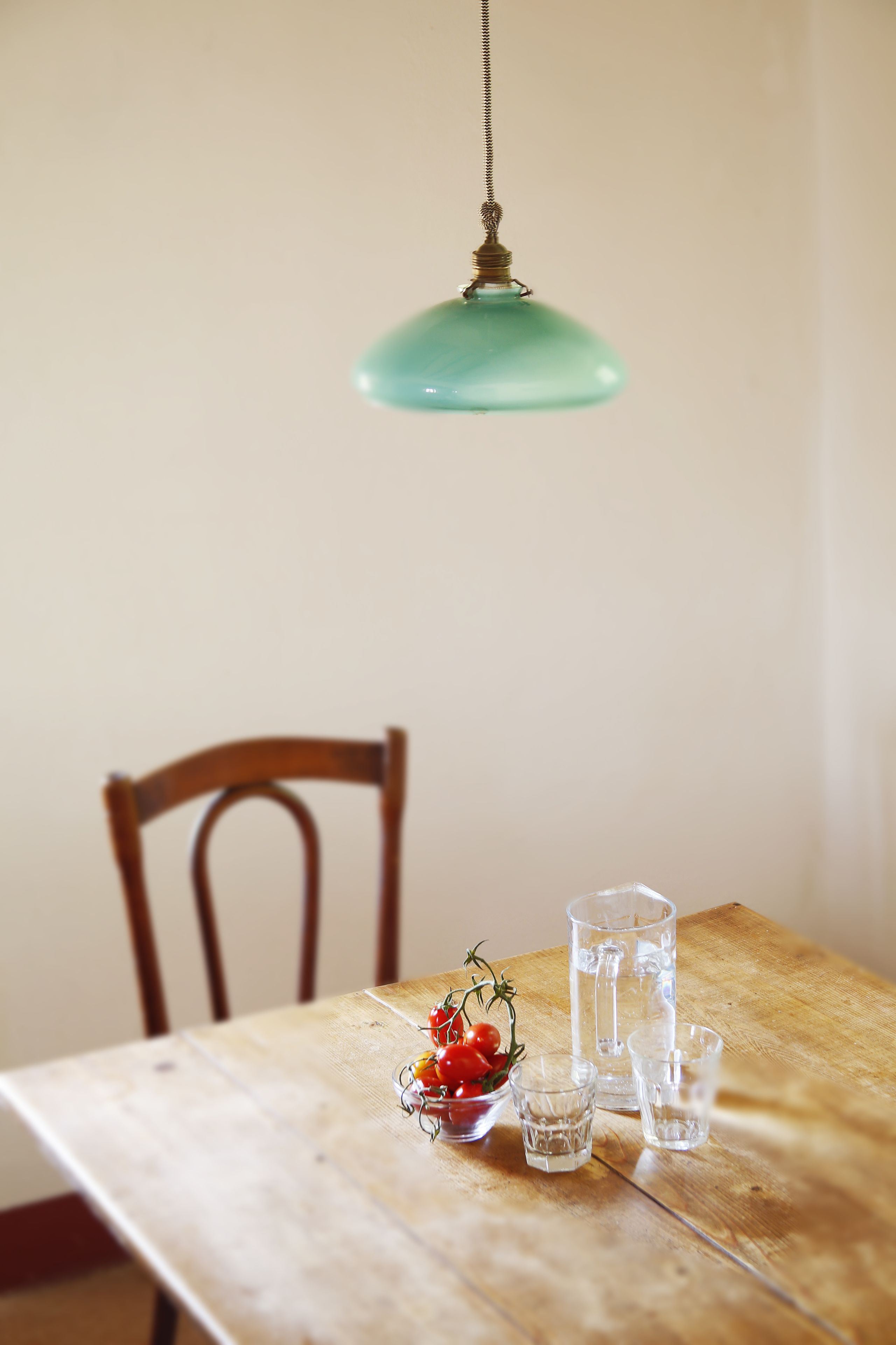 A wooden table with a glass pitcher, a glass, and a bowl of cherry tomatoes.