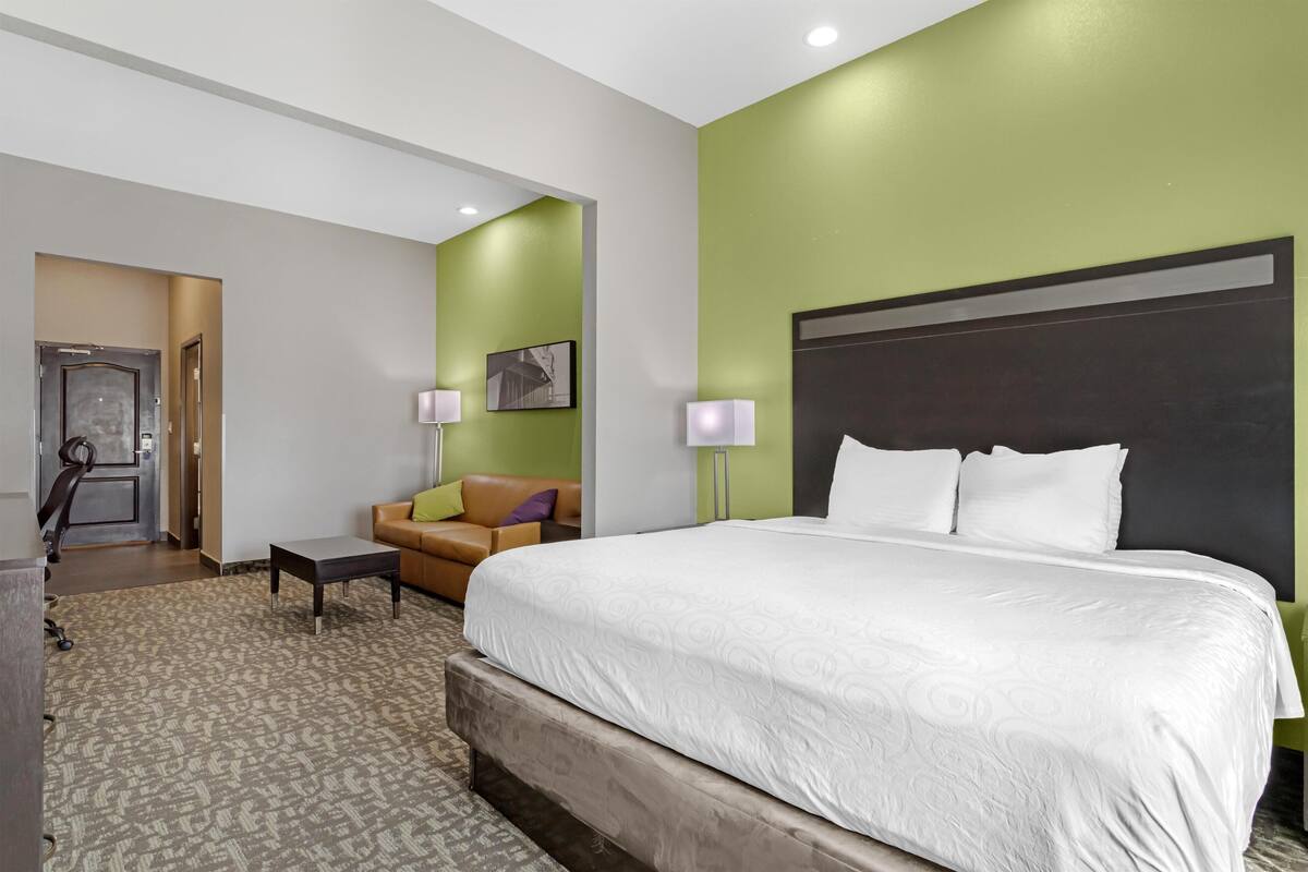A hotel room with a large bed, a sofa, a desk, and a door leading to a bathroom.