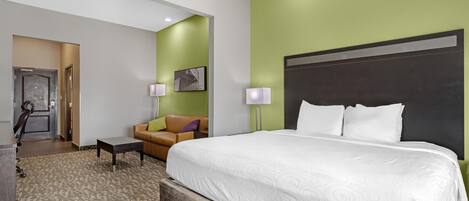 A hotel room with a large bed, a sofa, a desk, and a door leading to a bathroom.