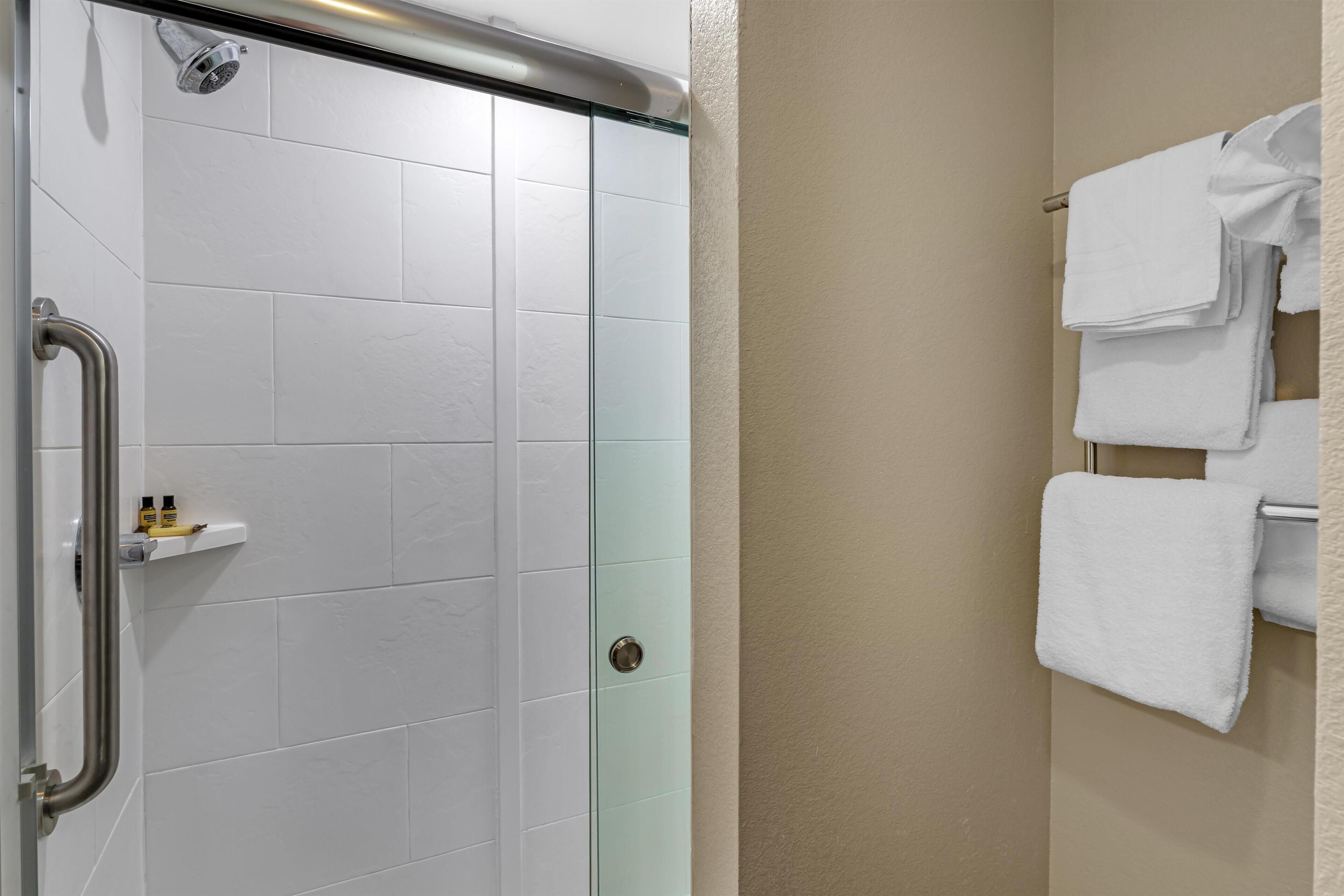 A bathroom with a glass shower door, a white towel rack, and a beige wall.