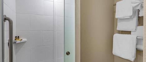 A bathroom with a glass shower door, a white towel rack, and a beige wall.
