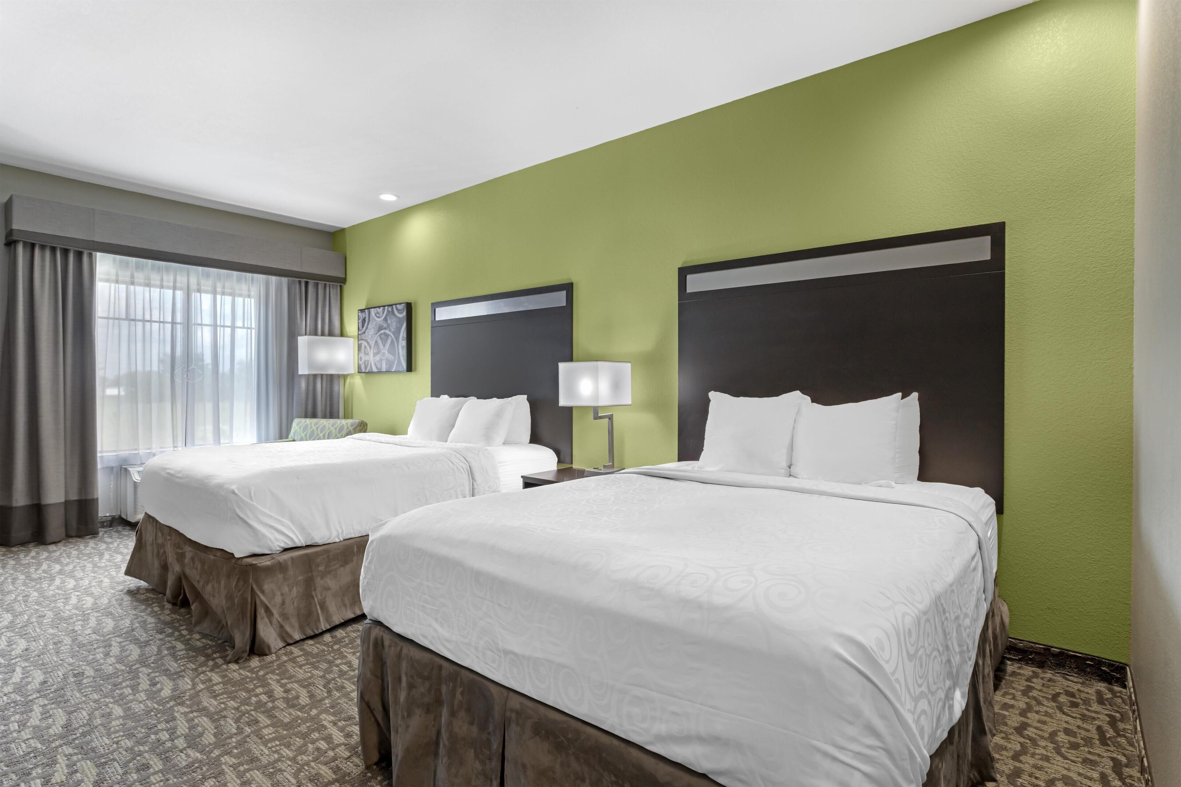 Habitación de hotel con dos camas, paredes verdes y alfombra estampada.
