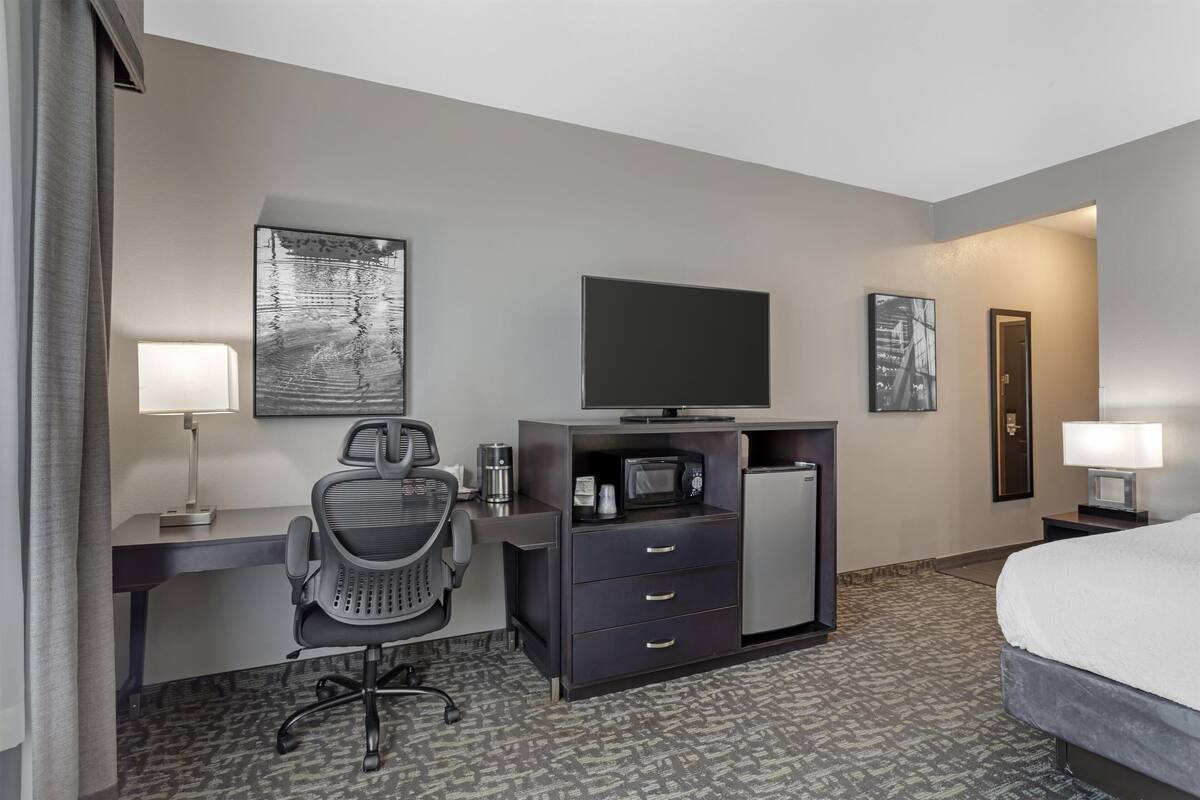 A hotel room with a bed, desk, chair, television, microwave, refrigerator, and artwork on the walls.