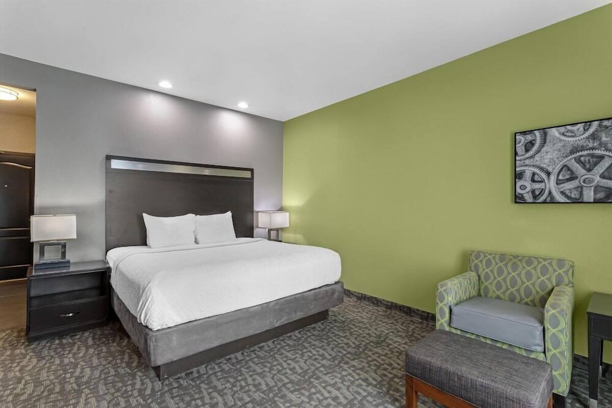 A hotel room with a bed, bedside tables, a chair, and a wall art piece.