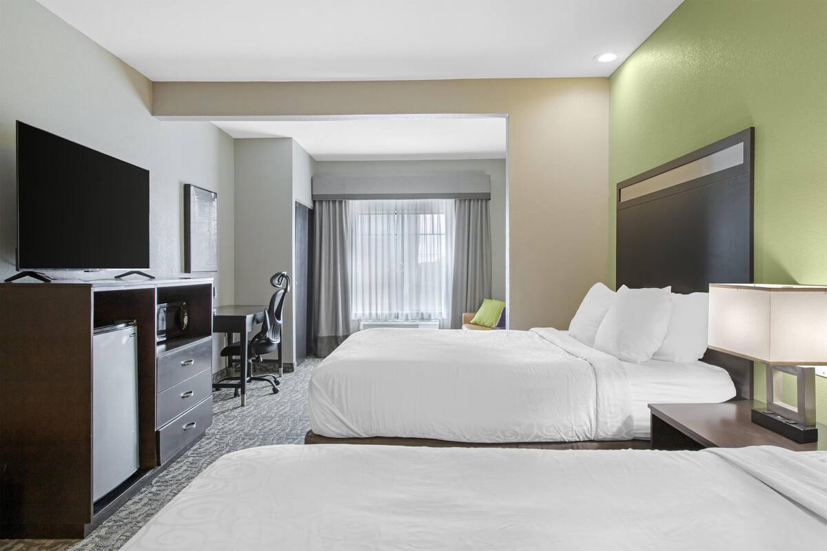 A hotel room with two beds, a desk, a chair, a TV, and a window with curtains.