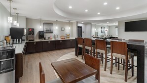 A modern kitchen with dark cabinets, a central island, and a dining area with wooden chairs and a table. - Best Western Plus Bay City Inn & Suites (Bay City)
