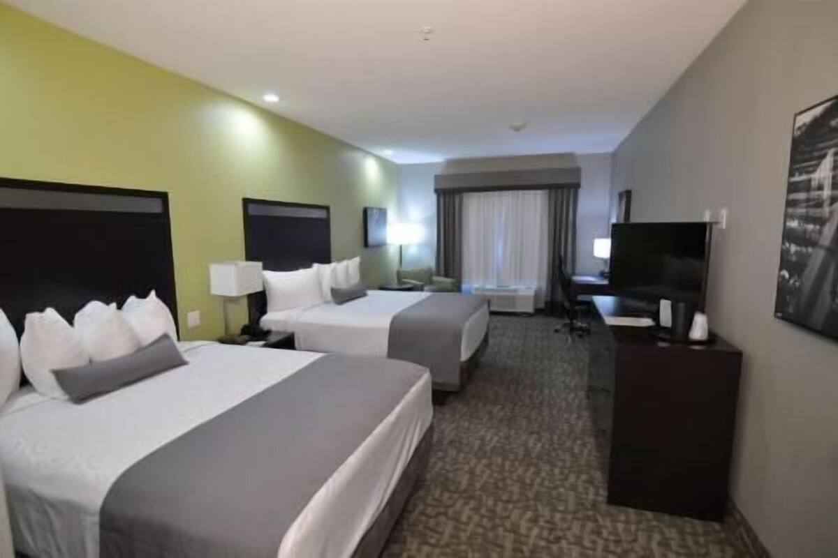 A hotel room with two beds, a desk with a TV, and a window with curtains.