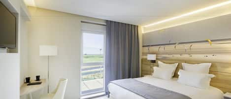 A modern hotel room with a large bed, a desk, a chair, and a view of the outdoors.