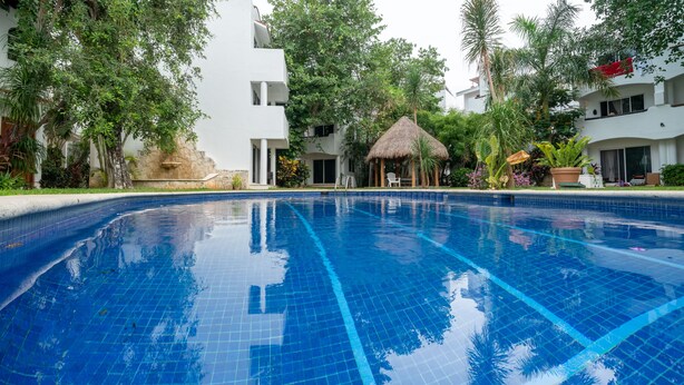 A swimming pool with clear blue tiles, surrounded by lush greenery and modern buildings. - Quintas Pakal 21 by NAS (Playa del Carmen)