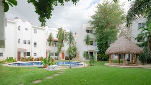 A courtyard with a swimming pool, a thatched gazebo, and white buildings with arched windows. - Quintas Pakal 21 by NAS (Playa del Carmen)