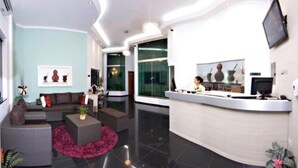 A modern hotel lobby with a reception desk, seating area, and a large window offering a view of the outdoors. - Herval Park Hotel (Ponta Pora)