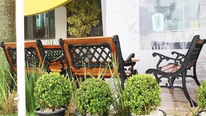 A patio area with wooden and black wrought iron chairs, potted plants, and a yellow awning. - Herval Park Hotel (Ponta Pora)