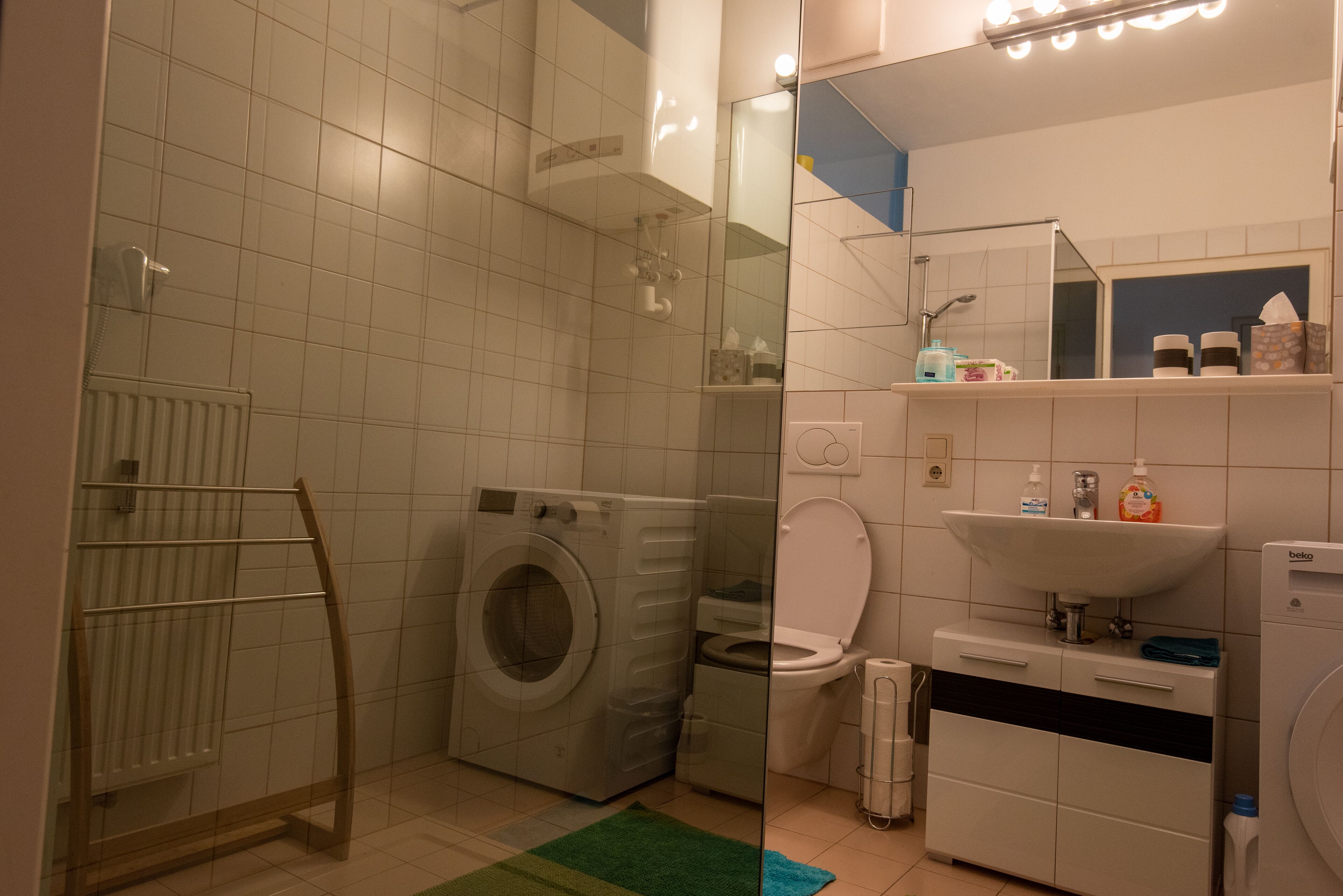 A bathroom with a washing machine, a toilet, a radiator, and a sink.