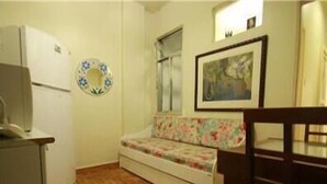 A compact kitchen with a refrigerator, a wooden herringbone floor, a floral-patterned bench, and a framed artwork on the wall. - GoHouse Copacabana 1203 (Rio de Janeiro)