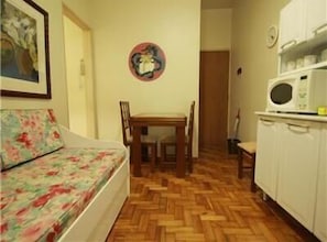 A small, cozy room with a wooden herringbone floor, a floral sofa, a dining table with chairs, and a microwave on a cabinet. - GoHouse Copacabana 1203 (Rio de Janeiro)