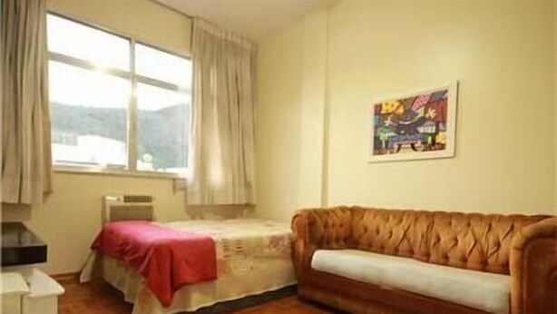 A room with a bed, a sofa, a window with curtains, and a painting on the wall. - GoHouse Copacabana 1203 (Rio de Janeiro)