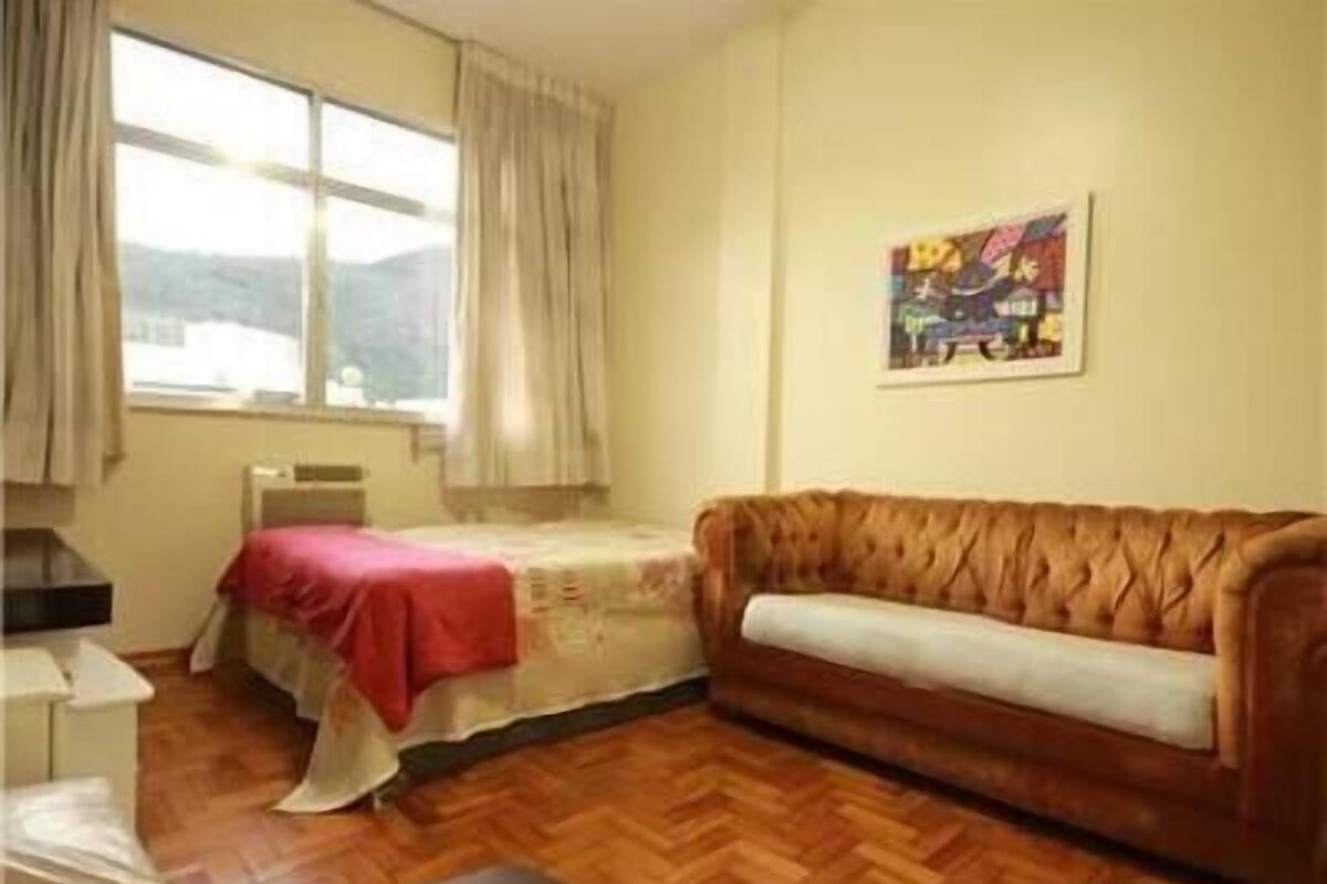 Une pièce avec un lit, un canapé, une fenêtre avec des rideaux et un tableau au mur.
