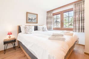Une chambre à coucher avec un grand lit, une table de chevet avec une lampe, un tableau encadré au mur et une fenêtre avec des rideaux.