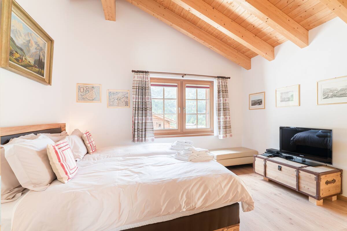 A bedroom with a large bed, a wooden headboard, a television, and a window with curtains.