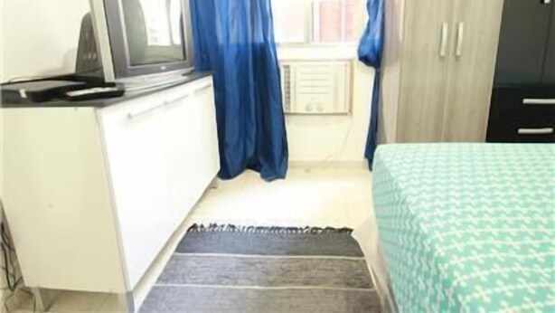 A small room with a bed, a desk with a computer, and a window with blue curtains.