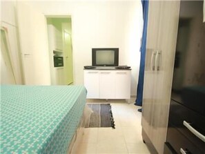 A small, compact room with a bed, a television on a cabinet, and a refrigerator.
