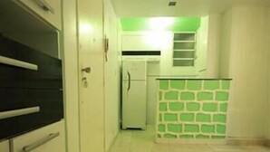 A narrow hallway with a kitchen area featuring a refrigerator and a green accent wall.