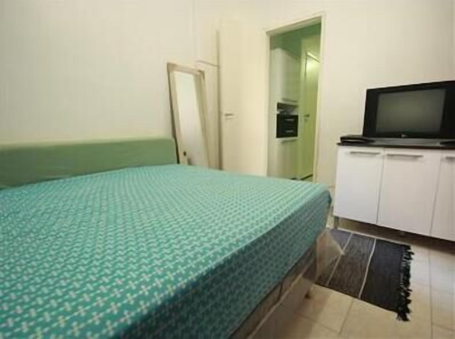 Ein Zimmer mit einem Bett, einem Fernseher auf einem Schrank und einer Tür zu einem weiteren Raum.
