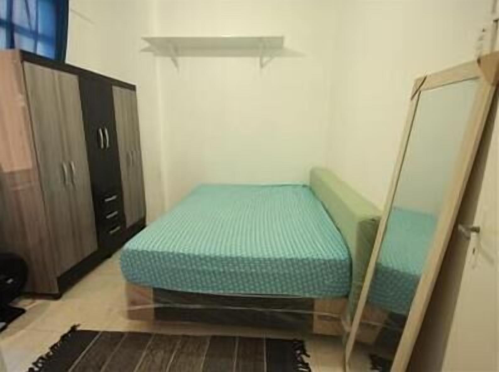 Ein kleines Zimmer mit einem Einzelbett, einem Holzschrank, einem Spiegel und einem Regal über dem Bett.