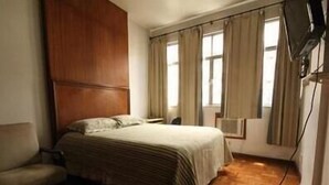 Ein Schlafzimmer mit einem hölzernen Kopfteil, einem Bett mit gestreifter Bettdecke, einem Sessel und einem an der Wand befestigten Fernseher.