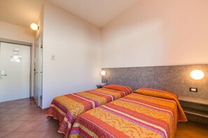 A bedroom with two beds, a headboard, a bedside table, a phone, and a door.