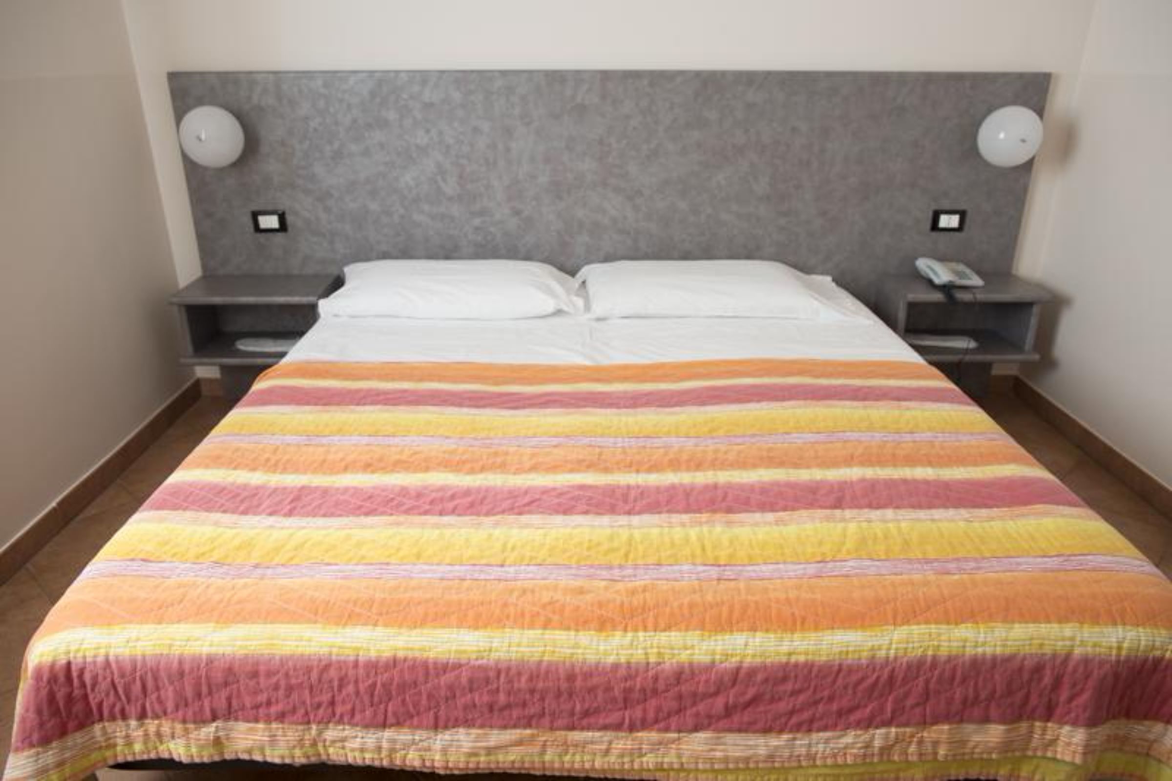 Una habitación de hotel con una cama grande, dos mesitas de noche y un cabecero.
